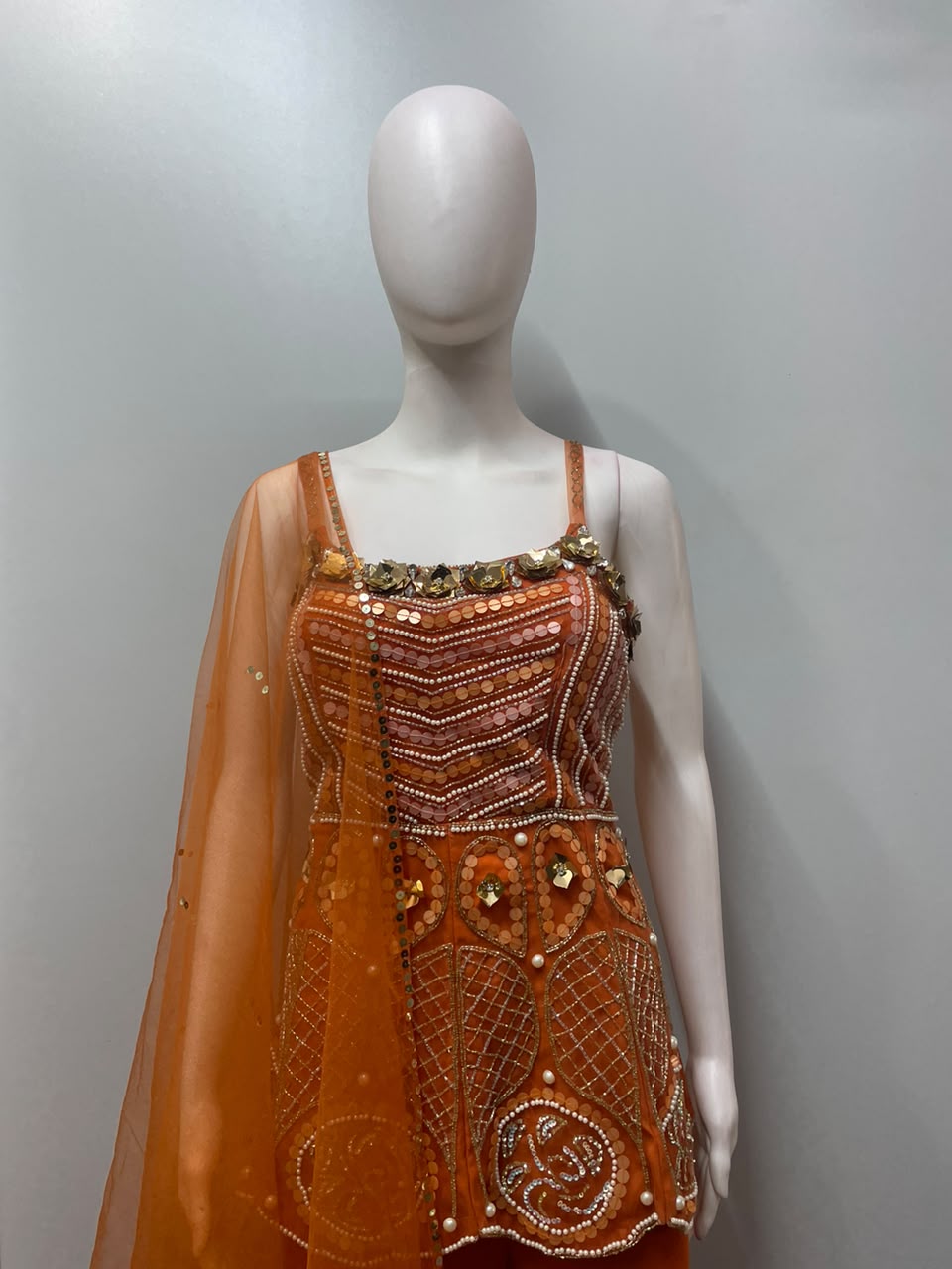 Detail of the peplum hem on a tangerine mirror embellished top